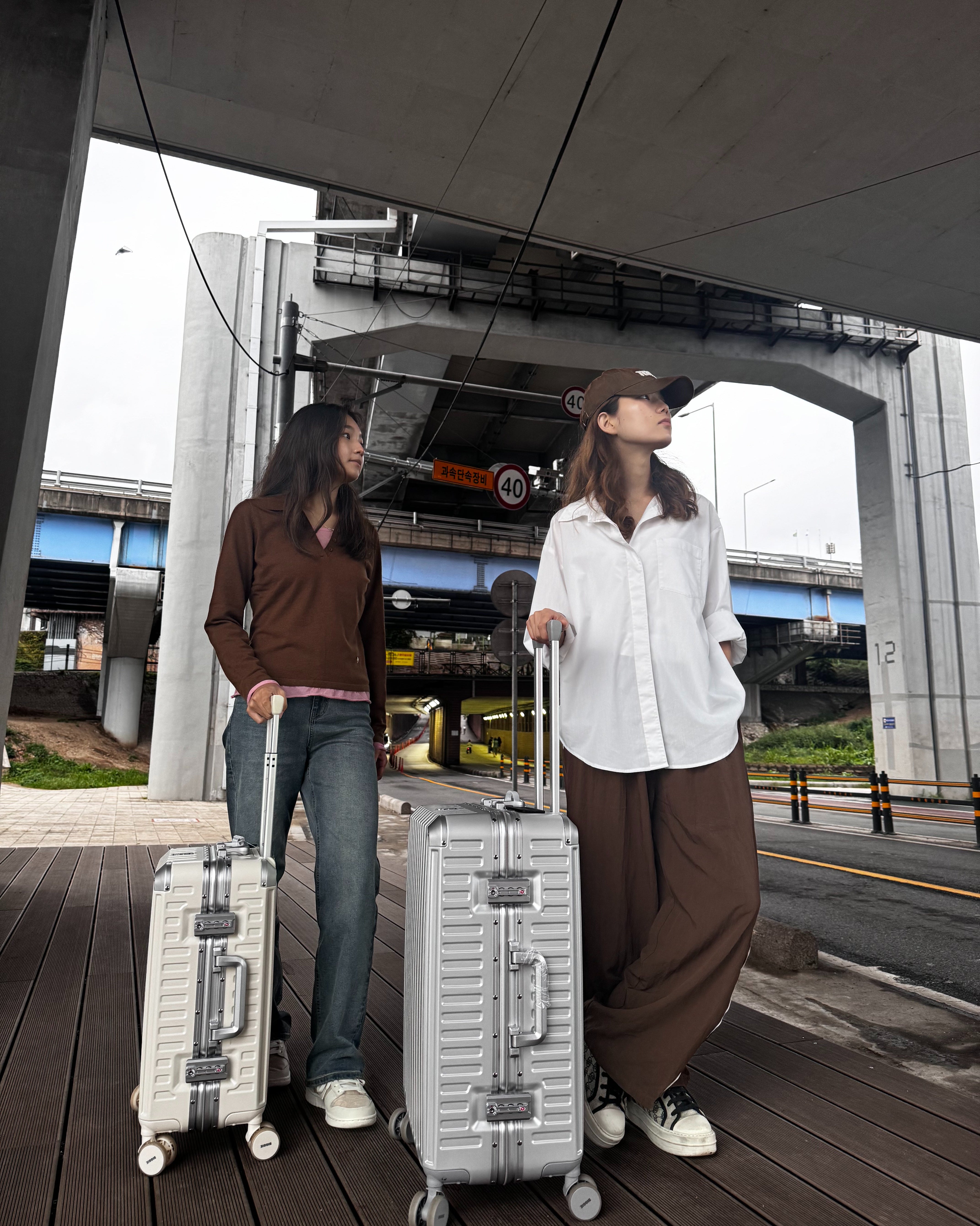 Two people with suitcases standing on a platform with a bridge in the background