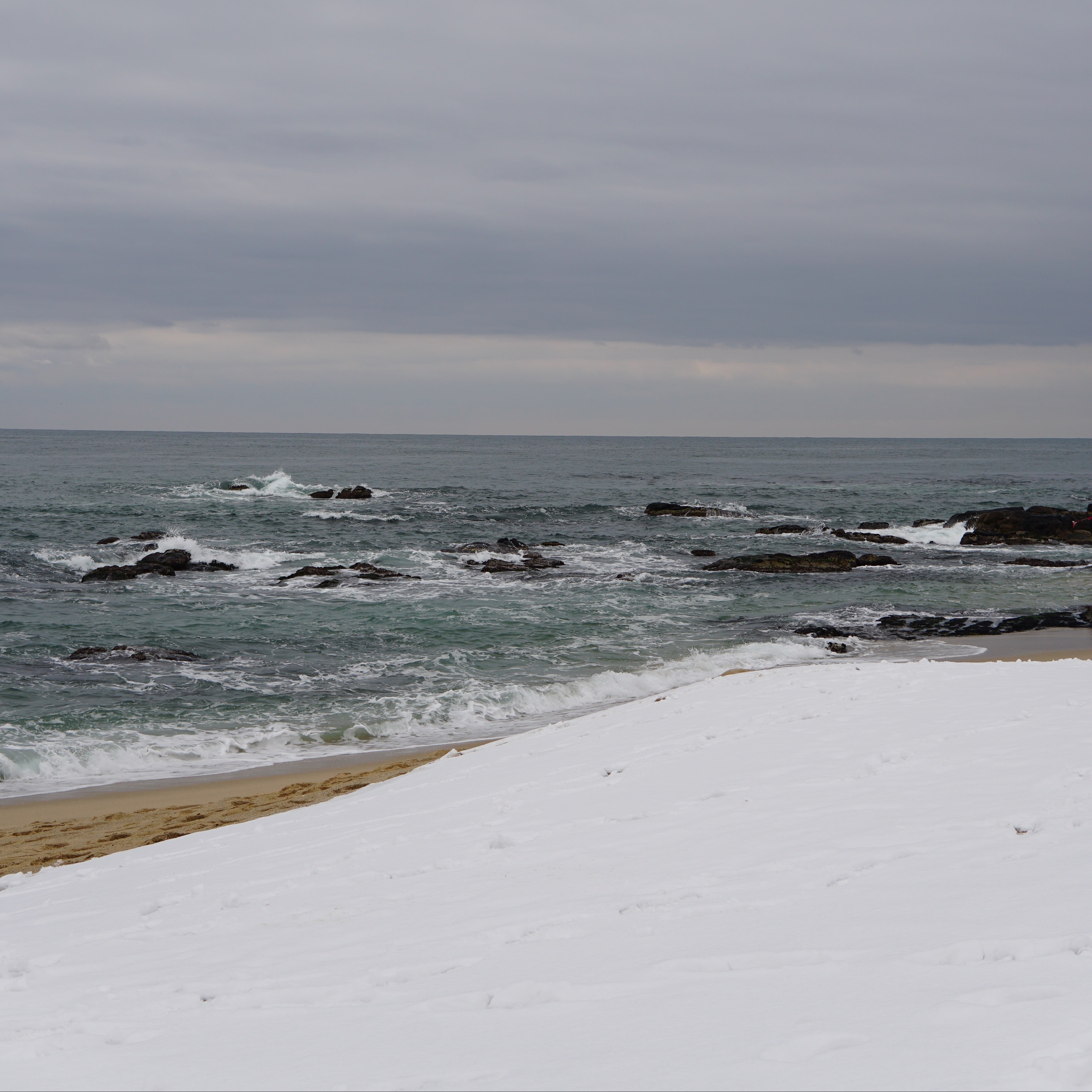 Coastline with waves crashing against rocks under a cloudy sky.